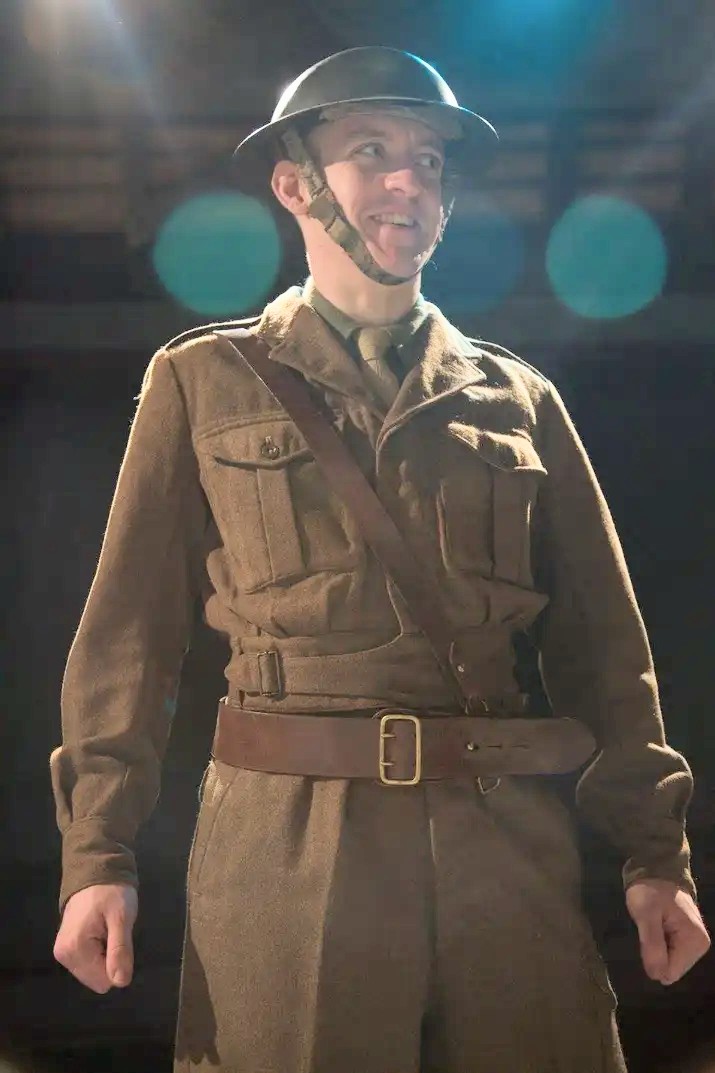 colour photo. tommo stands in british first world war soldier uniform, looking at a point off camera. he is smiling.
